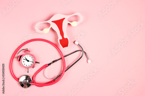 Women's health awareness concept. Uterus symbol with stethoscope and alarm clock on pink background. photo