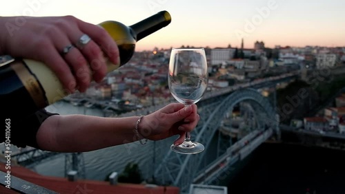 Authentic shot of unrecognizable hand pouring red wine to the glass. Oporto, Douro valley on the background. Enjoying red wine at Portugal, Porto, Port wine. Sunset colors on the background.