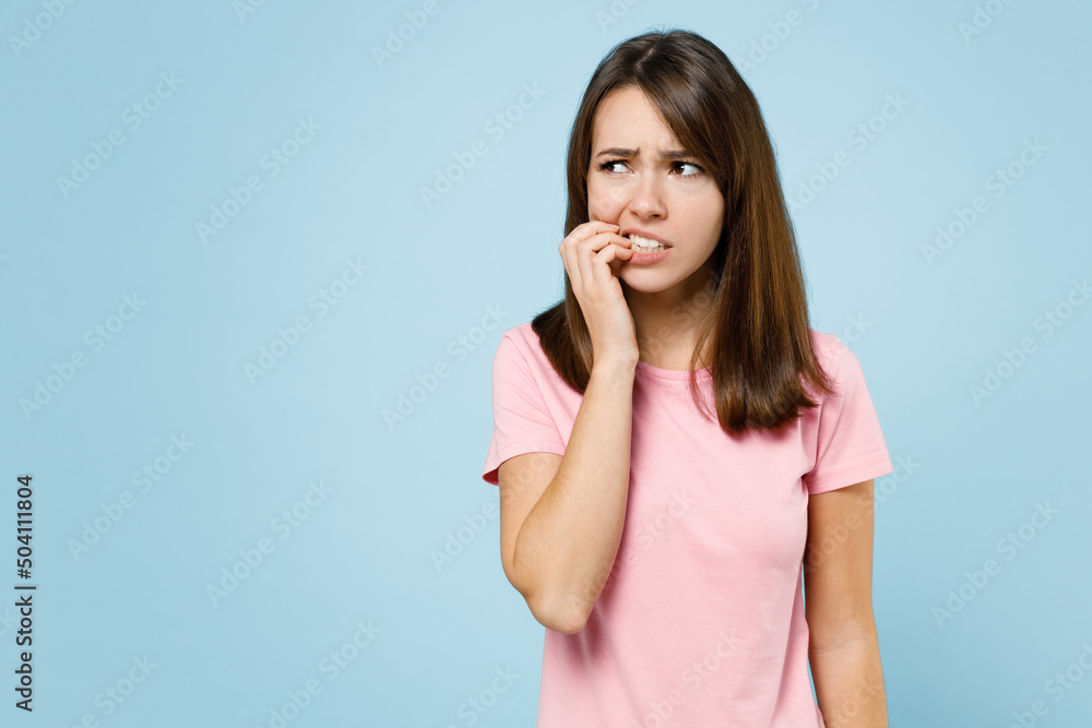 Young sad puzzled confused worried troubled caucasian woman 20s in pink t-shirt look aside biting nails fingers isolated on pastel plain light blue background studio portrait People lifestyle concept Young sad puzzled confused worried troubled caucasian woman 20s in pink t-shirt look aside biting nails fingers isolated on pastel plain light blue background studio portrait People lifestyle concept
