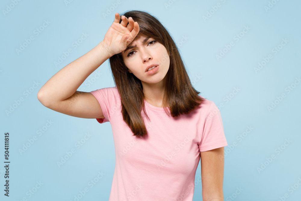 Young sad tired caucasian woman 20s wearing pink t-shirt look camera put hand on forehead suffer from headache isolated on pastel plain light blue background studio portrait. People lifestyle concept.