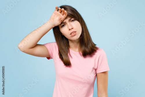 Young sad tired caucasian woman 20s wearing pink t-shirt look camera put hand on forehead suffer from headache isolated on pastel plain light blue background studio portrait. People lifestyle concept.