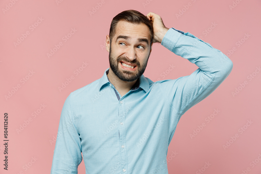 Young puzzled caucasian man 20s wear classic blue shirt look aside on workspace area mock up scratch hold head isolated on plain pastel light pink background studio portrait. People lifestyle concept. Young puzzled caucasian man 20s wear classic blue shirt look aside on workspace area mock up scratch hold head isolated on plain pastel light pink background studio portrait. People lifestyle concept.