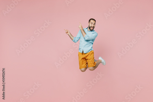Full body young excited fun man 20s wear classic blue shirt jump high point index finger aside on workspace area mock up isolated on plain pastel light pink background studio People lifestyle concept © ViDi Studio