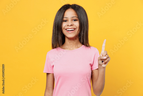 Little kid girl of African American ethnicity 12-13 years old in pink t-shirt hold index finger up with great new idea isolated on plain yellow background studio portrait. Childhood lifestyle concept.