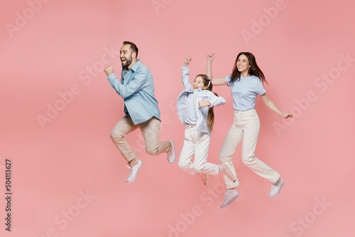 Full size young happy fun parents mom dad with child kid daughter teen girl in blue clothes jump high do winner gesture clench fist isolated on plain pastel light pink background. Family day concept.