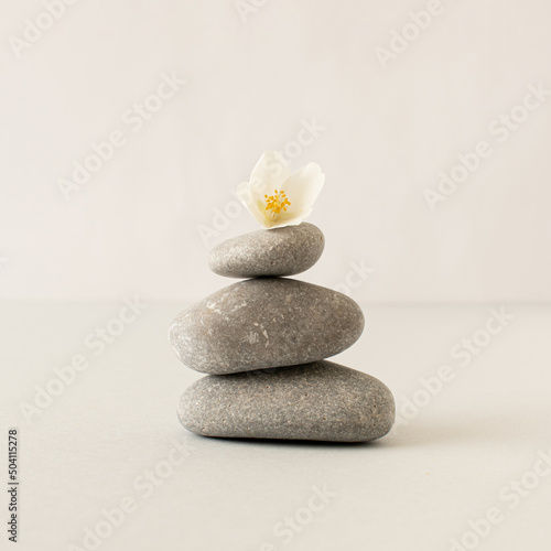 Gray pebbles and white flower on bright background. Zen like concept. Stone spa concept.