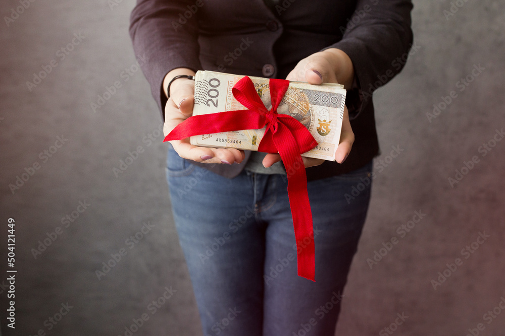 Kobieta trzyma w rękach dużo polskich pieniędzy przewiązanych czerwoną wstążką - obrazy, fototapety, plakaty 