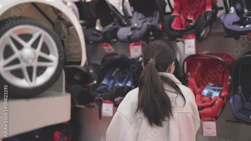 Asian woman in white choosing car seats in supermarket with stroller