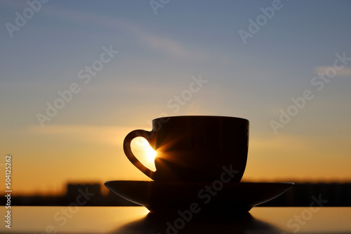 Black silhouette of coffee or tea cup on sunset sky background. View from the window to evening city