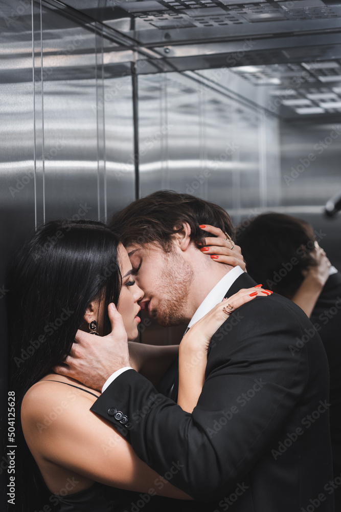 Sexy woman kissing boyfriend in suit in elevator.