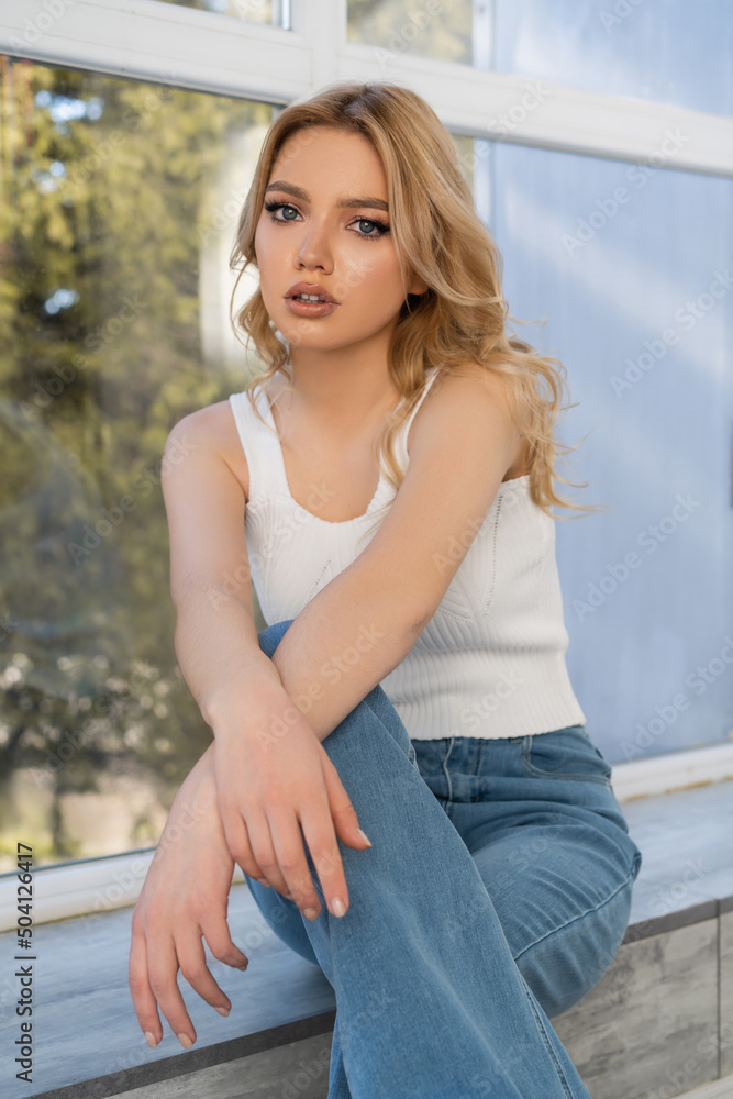 young woman in jeans sitting near window and looking at camera. young woman in jeans sitting near window and looking at camera.