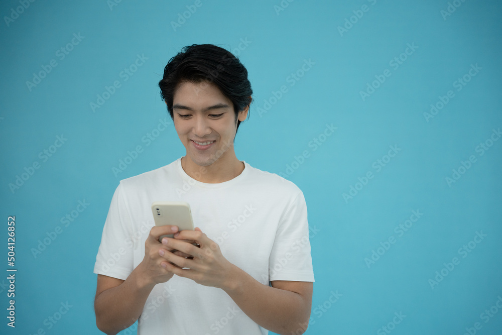Handsome Asian man smiling happy with his phone on light blue background. Handsome Asian man smiling happy with his phone on light blue background.