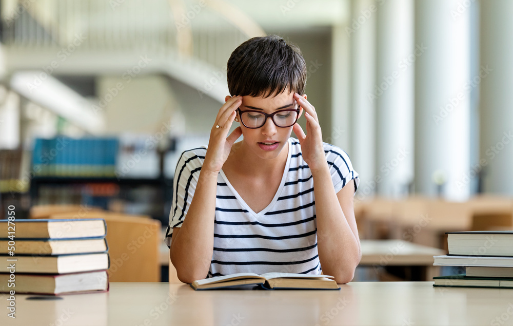 Exhausted young female studying and preparing for exam in college library. Education people concept Exhausted young female studying and preparing for exam in college library. Education people concept