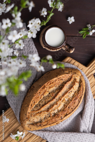 Fresh homemade rye cereal bread with clay mug of milk on wooden cutting board. Healthy breakfast