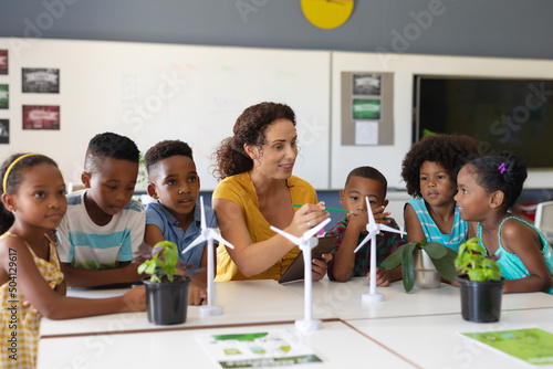 African american elementary students listening to caucasian young female teacher showing windmill