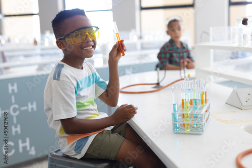 Portrait of smiling african american elementary schoolboy showing test tube during chemistry class