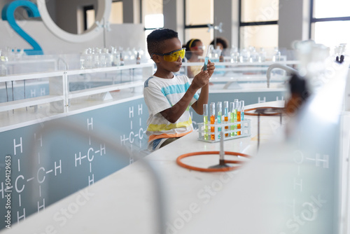 African american elementary schoolboy looking at chemical in test tube during chemistry class