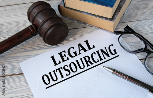 LEGAL OUTSOURCING - words on white paper with the background of the judge's hammer, glasses and pen