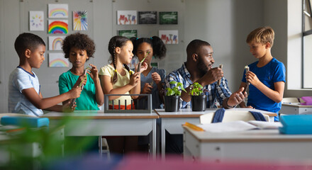 Multiracial elementary students and african american young male teacher discussing on plant in class