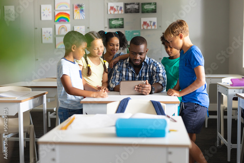 African american young male teacher showing digital tablet to multiracial elementary students
