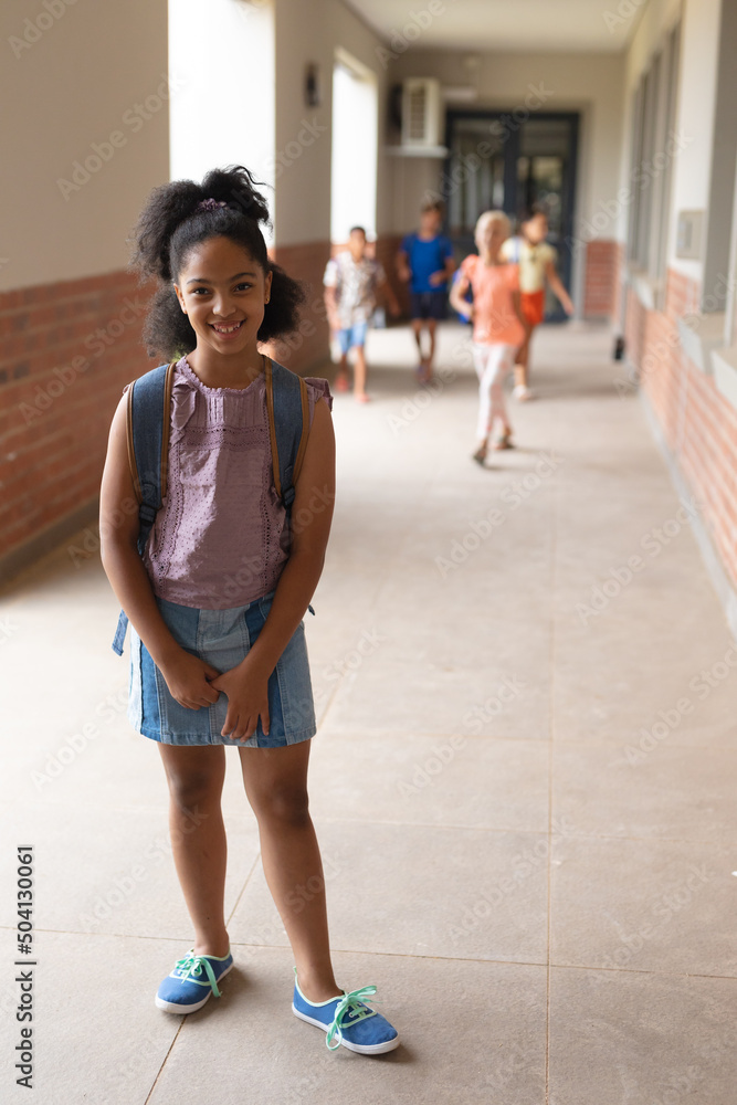 Portrait of smiling biracial elementary schoolgirl standing in corridor