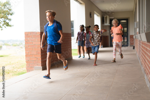 Multiracial elementary school students running in school corridor