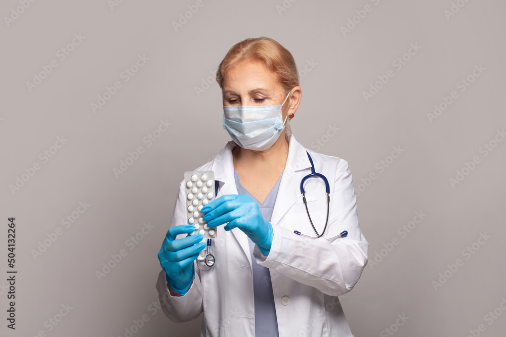 Female pharmacist explain about how to use drug, she holding pills strip pack with her hand on gray background Female pharmacist explain about how to use drug, she holding pills strip pack with her hand on gray background