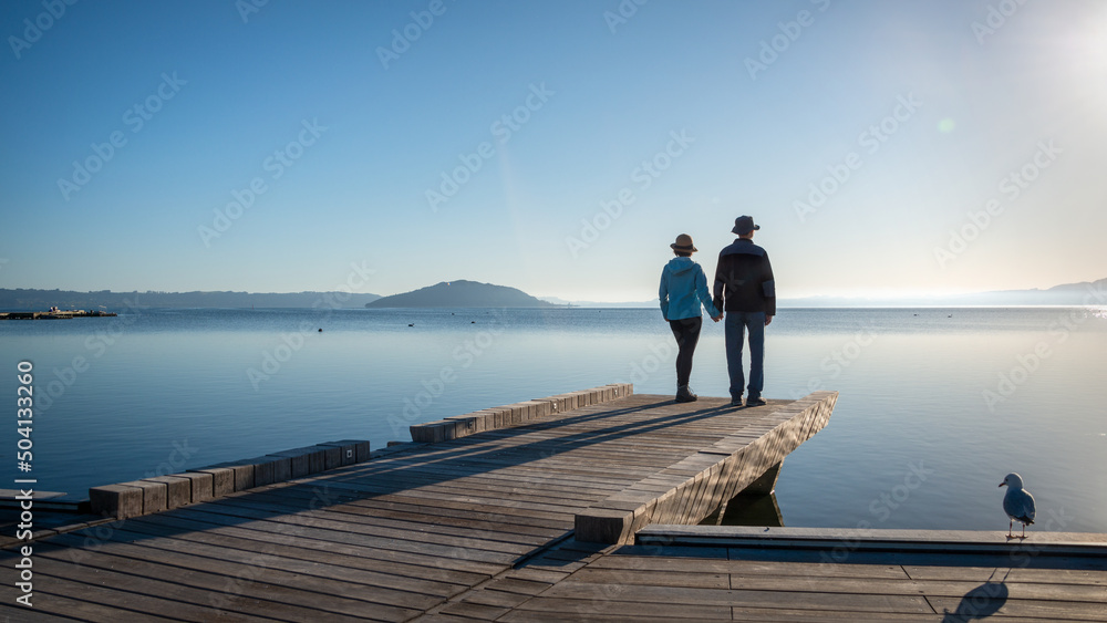 Fototapeta premium Couple holding hands, standing on the lakefront boardwalk, Rotorua.