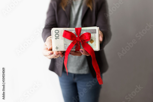 Kobieta trzyma w rękach dużo polskich pieniędzy przewiązanych czerwoną wstążką