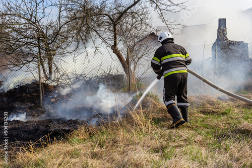 spring fire, burning dry grass near buildings in the countryside. Firefighter extinguishes the flame. Environmental disaster