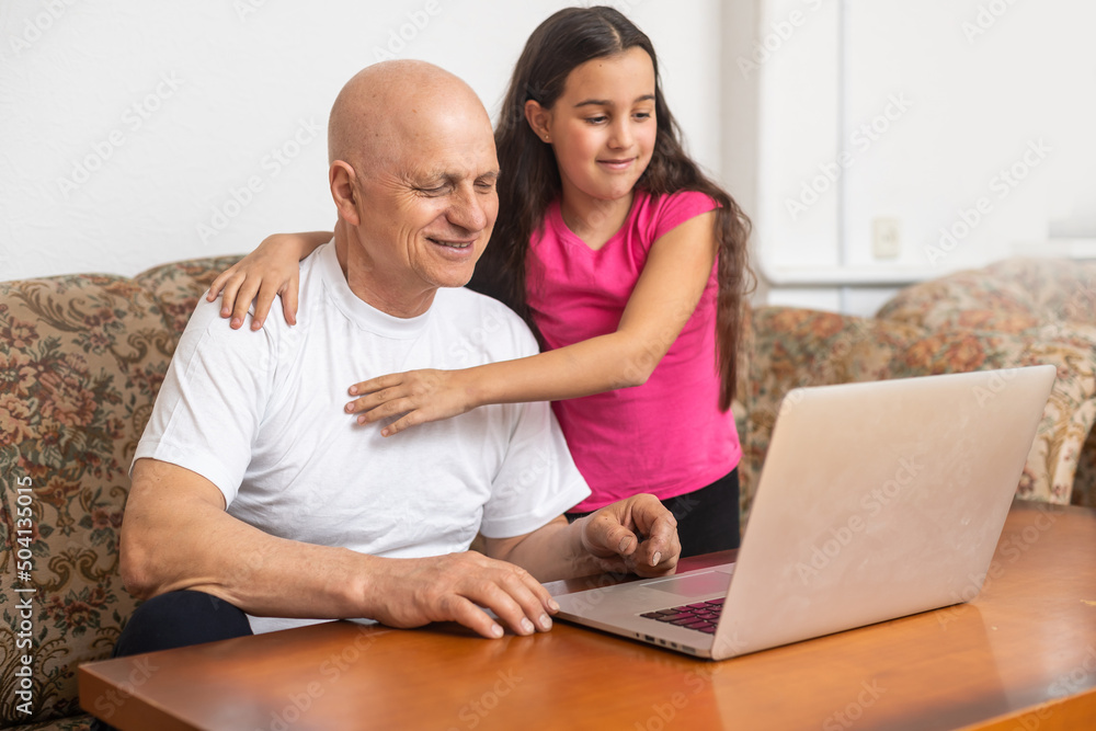 Adorable little girl hugging happy grandfather using laptop at home. Adorable little girl hugging happy grandfather using laptop at home.