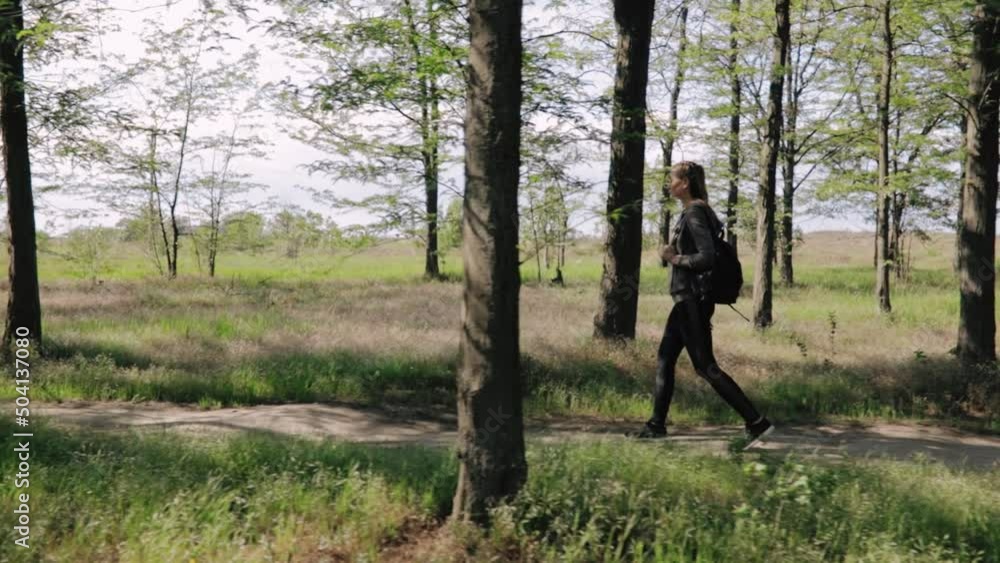 Young woman in sportswear with backpack among green trees going to stadium to make physical exercises. Young woman in sportswear with backpack among green trees going to stadium to make physical exercises.