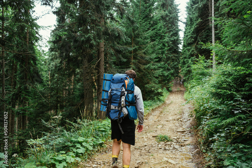 Back of a male tourist with a backpack on his back walks along a path in the mountains ahead.