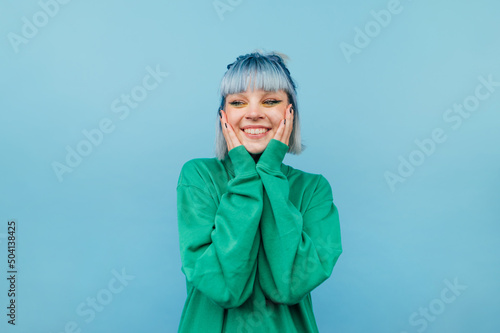 Joyful girl with blue hair stands on a green background with a smile on his face and happy looks away.