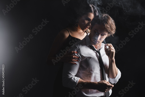 Sexy woman hugging boyfriend with cigarette on black background.