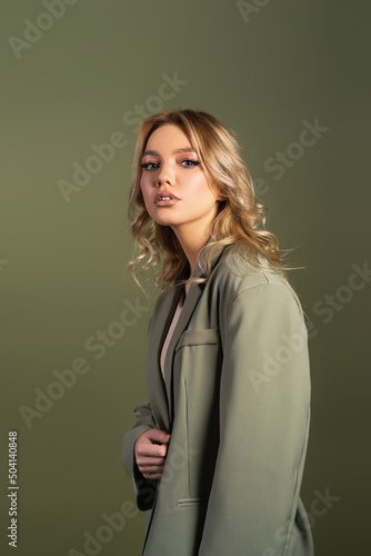 pretty woman with wavy hair posing in oversize blazer isolated on green.