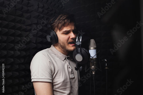 man sings into microphone, professional recording studio, headphones. Black soft walls, sound insulation. singer records his song.