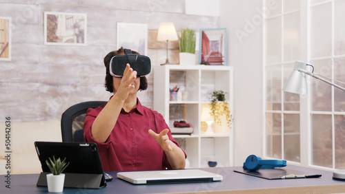 Elderly age woman using virtual reality goggles in living room. Old man sitting on sofa in the background.