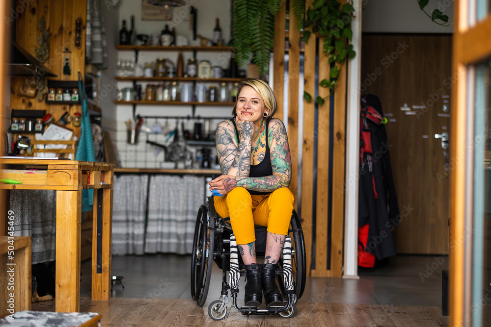 Obraz premium Portrait of an young tattooed woman in a wheelchair at home 