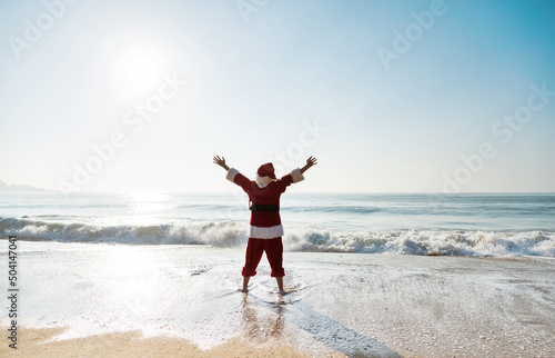 Santa claus standing on beach with arms outstretched.