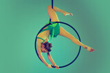 Portrait of young flexible girl, professional air gymnast training on hoop isolated over green background in neon light