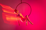 Young artistic girl, professional air gymnast training, performing isolated over pink background with mixed lights effect
