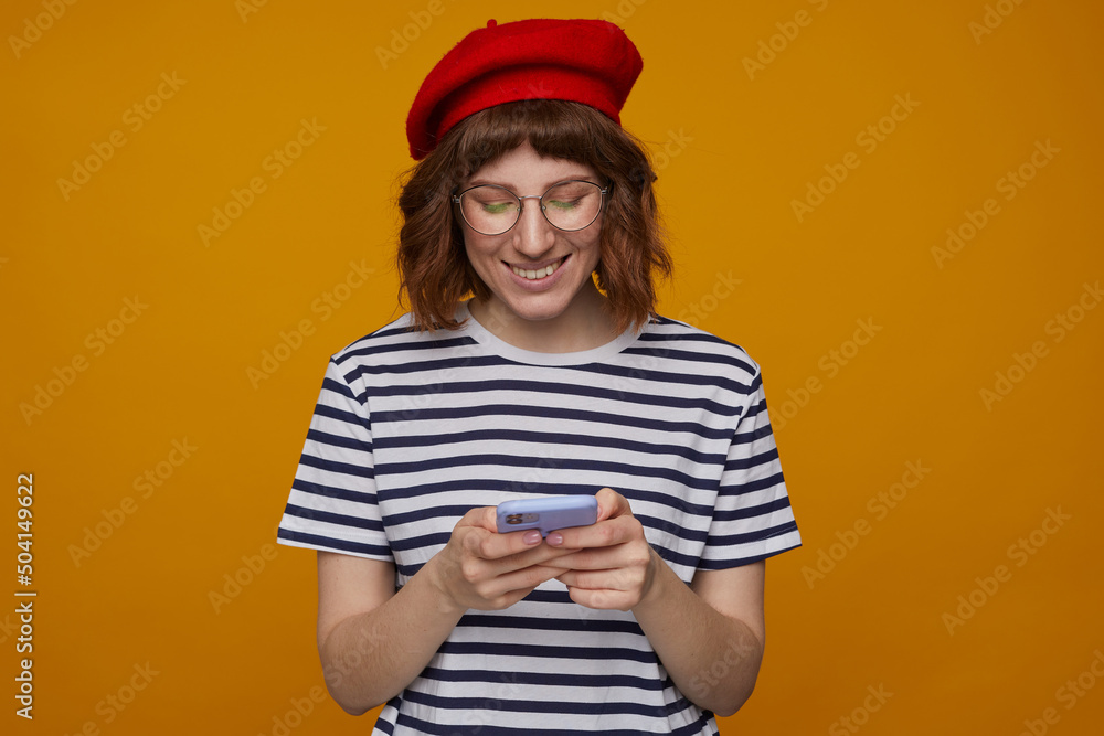 indoor portrait of young ginger female, wears stripped t shirt and glasses posing over orange background indoor portrait of young ginger female, wears stripped t shirt and glasses posing over orange background