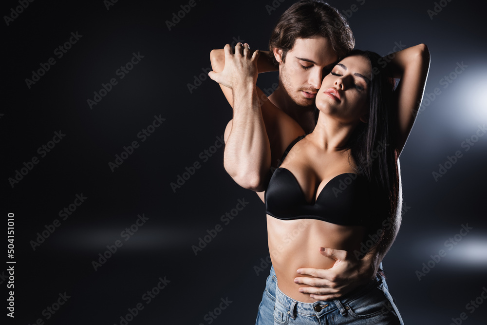 Young man touching sexy woman in bra on black background.