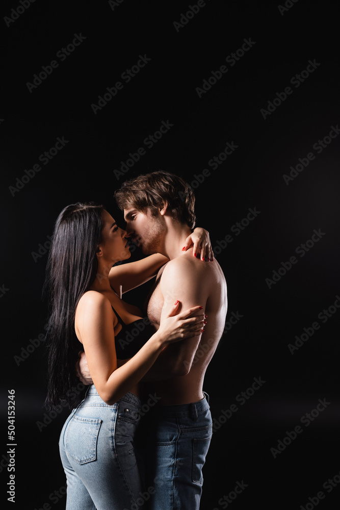 Fototapeta premium Side view of sexy couple in jeans kissing and hugging isolated on black.