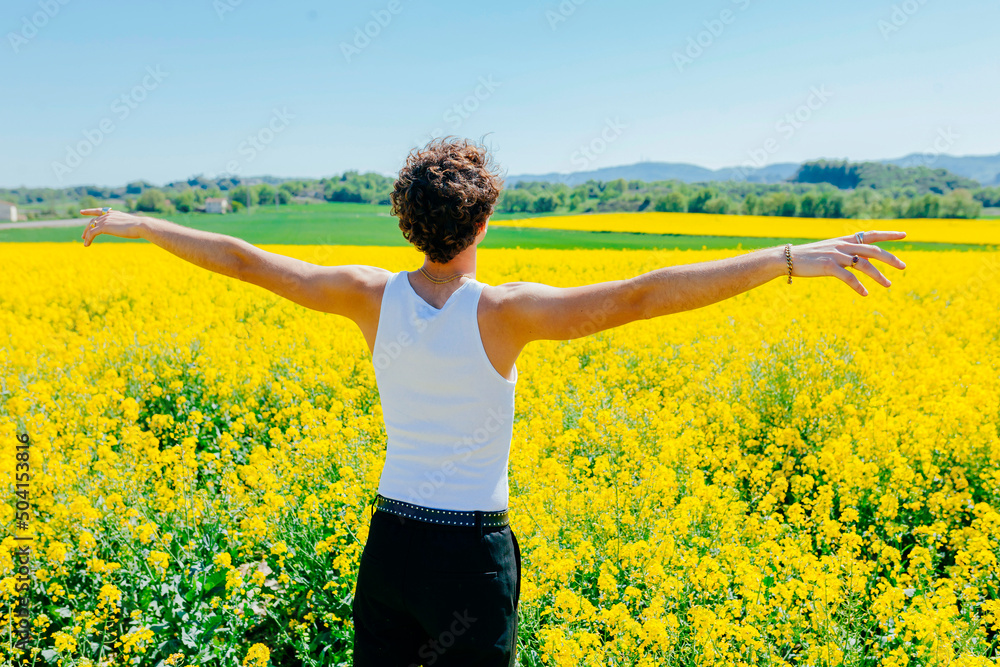 Rear view portrait of young man with open arms at the yellow field. Spring, summer vacations, happiness and good mood concept. Rear view portrait of young man with open arms at the yellow field. Spring, summer vacations, happiness and good mood concept.