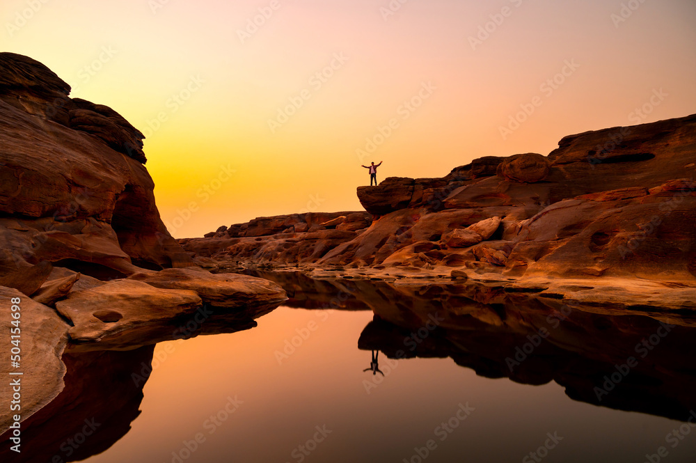 Minimal Man standing on the rock and reflection on water at Sunset Sam Phan BOK nation park ,Ubon ratchathani province,Thailand,ASIA.