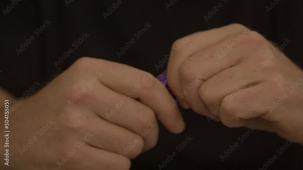 Male hands struggling to open purple condom package Male hands struggling to open purple condom package