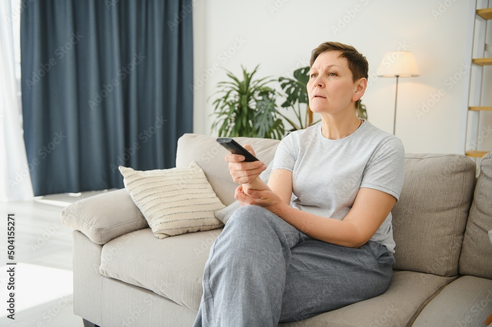 Woman sitting in living room holding remote control smiling. Woman sitting in living room holding remote control smiling.