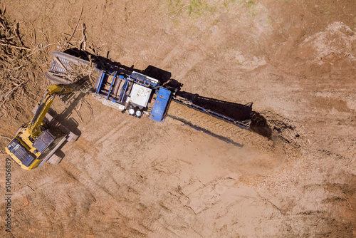 Conveyor of stationary industrial wood shredder producing wood chips on aerial top view photo